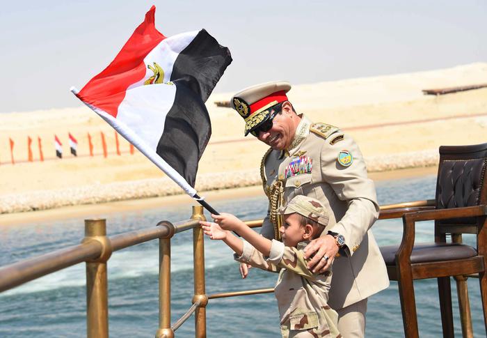 In this picture provided by the office of the Egyptian Presidency, Egyptian President Abdel-Fattah el-Sissi smiles at a boy dressed on a tiny military uniform as he waves the national flag from a monarchy-era yacht that sailed to the venue of a ceremony unveiling a major extension of the Suez Canal in Ismailia, Egypt, Thursday, Aug. 6, 2015. El-Sissi has billed the extension as an historic achievement needed to boost the countrys ailing economy after years of unrest. (Egyptian Presidency via AP) MANDATORY CREDIT